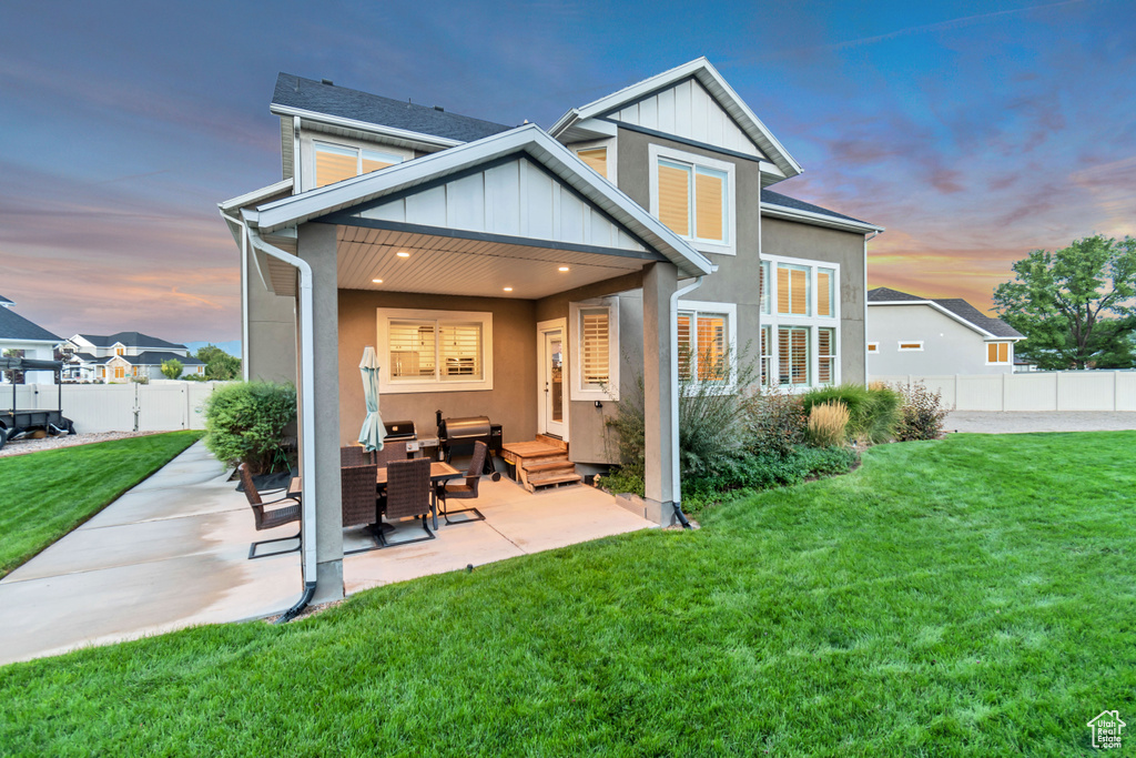 Back house at dusk with a lawn, an outdoor living space, and a patio