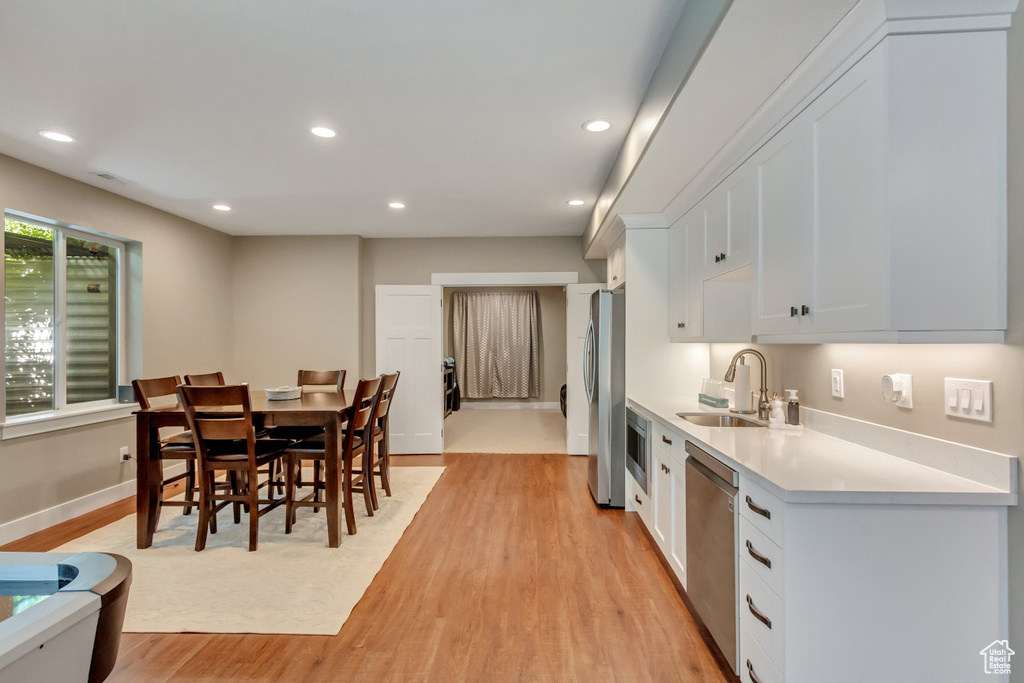 Kitchen with appliances with stainless steel finishes, sink, white cabinets, and light hardwood / wood-style floors