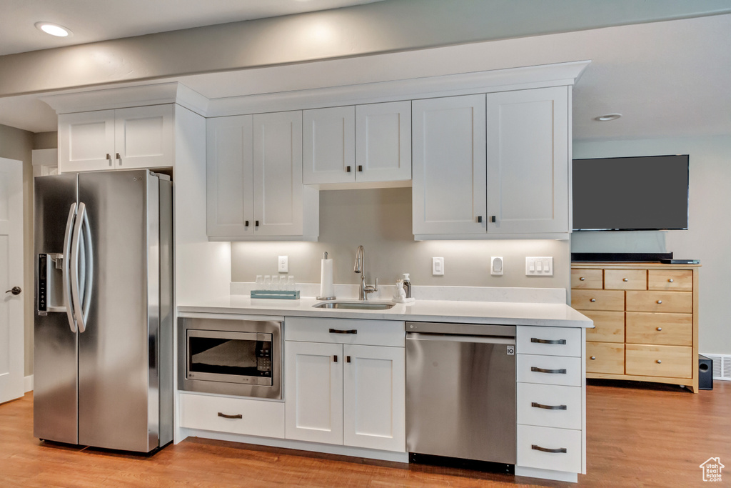 Kitchen with stainless steel appliances, sink, light wood-type flooring, and white cabinets