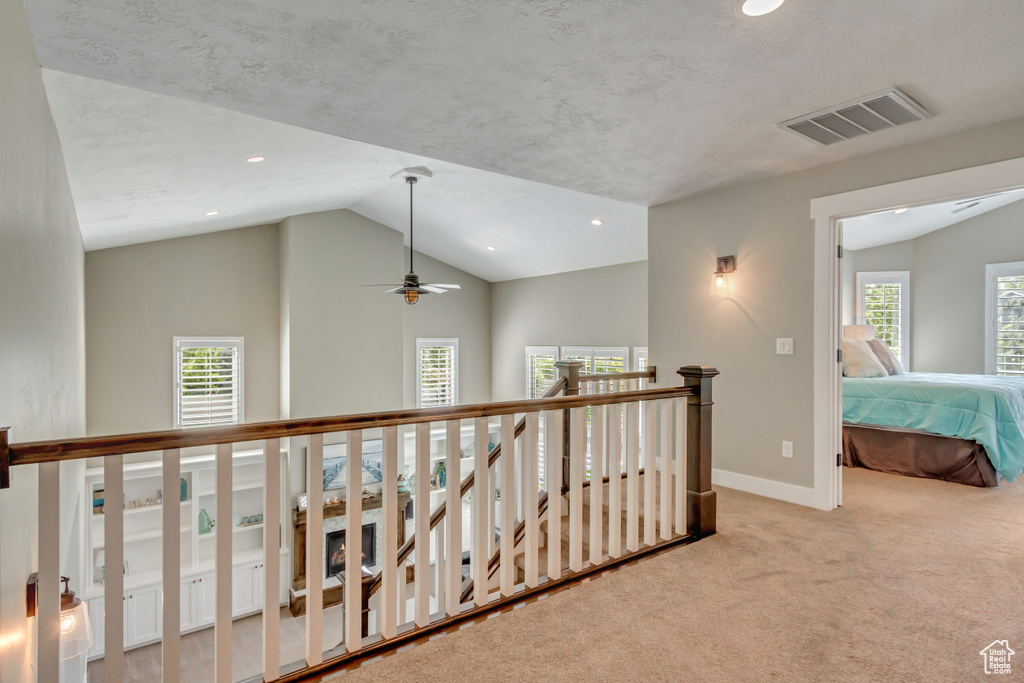 Hallway featuring light carpet, vaulted ceiling, and a textured ceiling