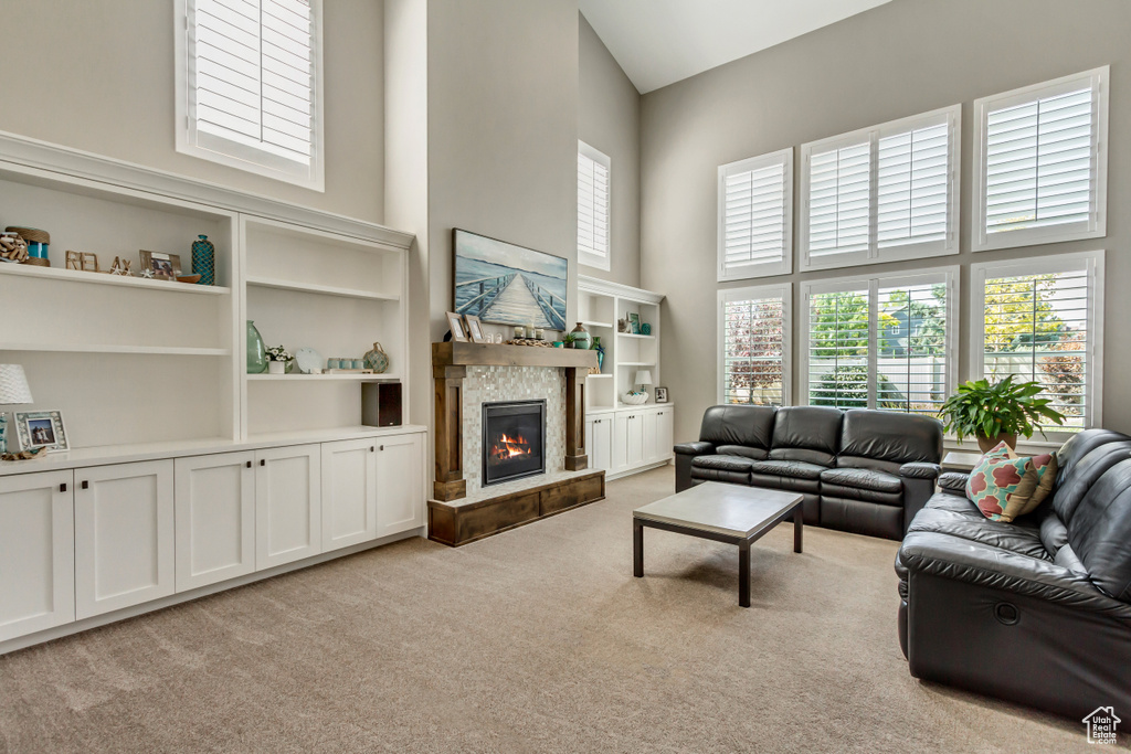 Living room with a high ceiling, built in shelves, light colored carpet, and a stone fireplace