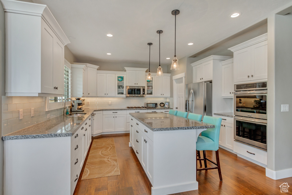 Kitchen with light wood-type flooring, a kitchen breakfast bar, a center island, sink, and appliances with stainless steel finishes