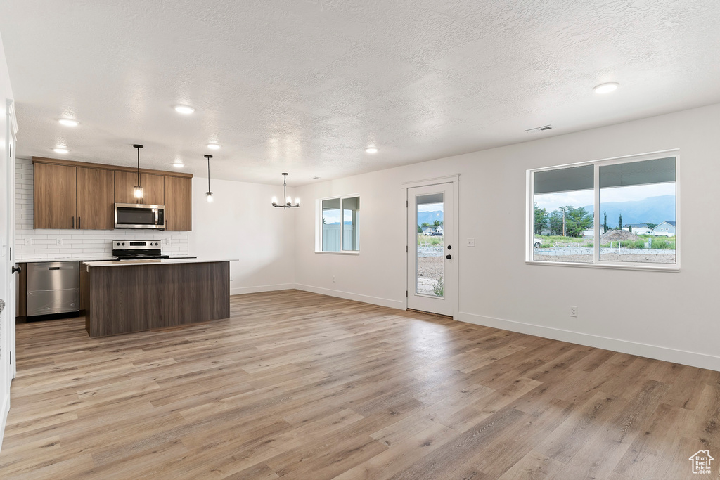 Kitchen with a textured ceiling, light hardwood / wood-style flooring, pendant lighting, and appliances with stainless steel finishes