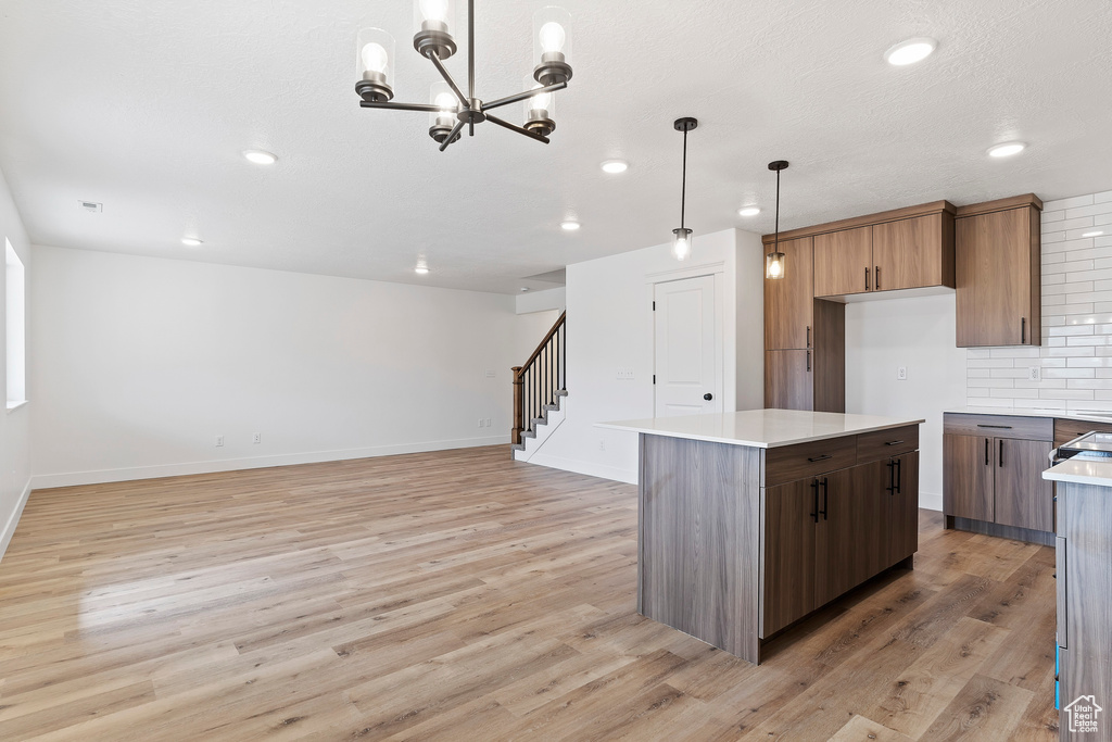 Kitchen with a notable chandelier, tasteful backsplash, light hardwood / wood-style flooring, a kitchen island, and hanging light fixtures