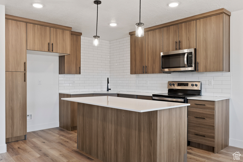 Kitchen with a textured ceiling, decorative light fixtures, light hardwood / wood-style flooring, a center island, and stainless steel appliances