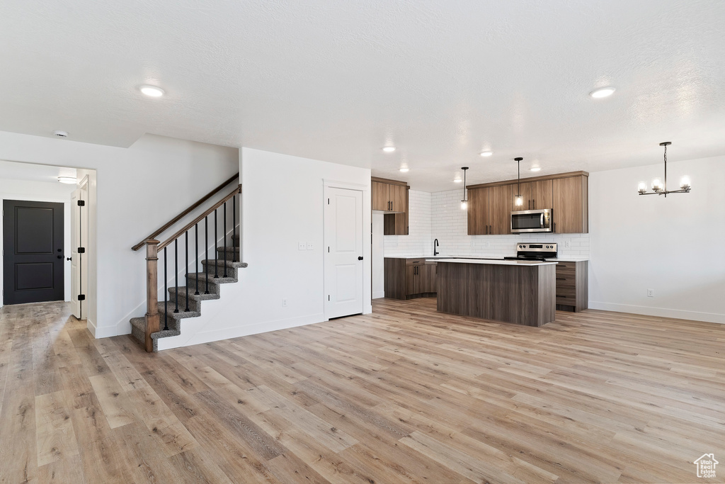 Kitchen featuring pendant lighting, backsplash, a kitchen island, appliances with stainless steel finishes, and light hardwood / wood-style floors