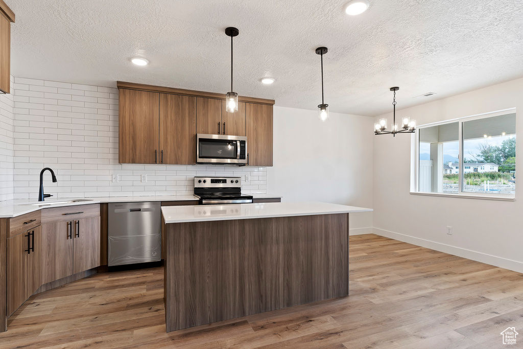 Kitchen featuring light wood-type flooring, appliances with stainless steel finishes, decorative light fixtures, and a notable chandelier