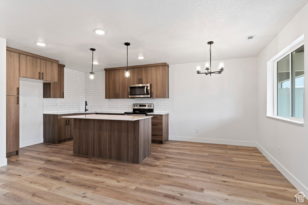 Kitchen featuring light wood-type flooring, a kitchen island, stainless steel appliances, and tasteful backsplash