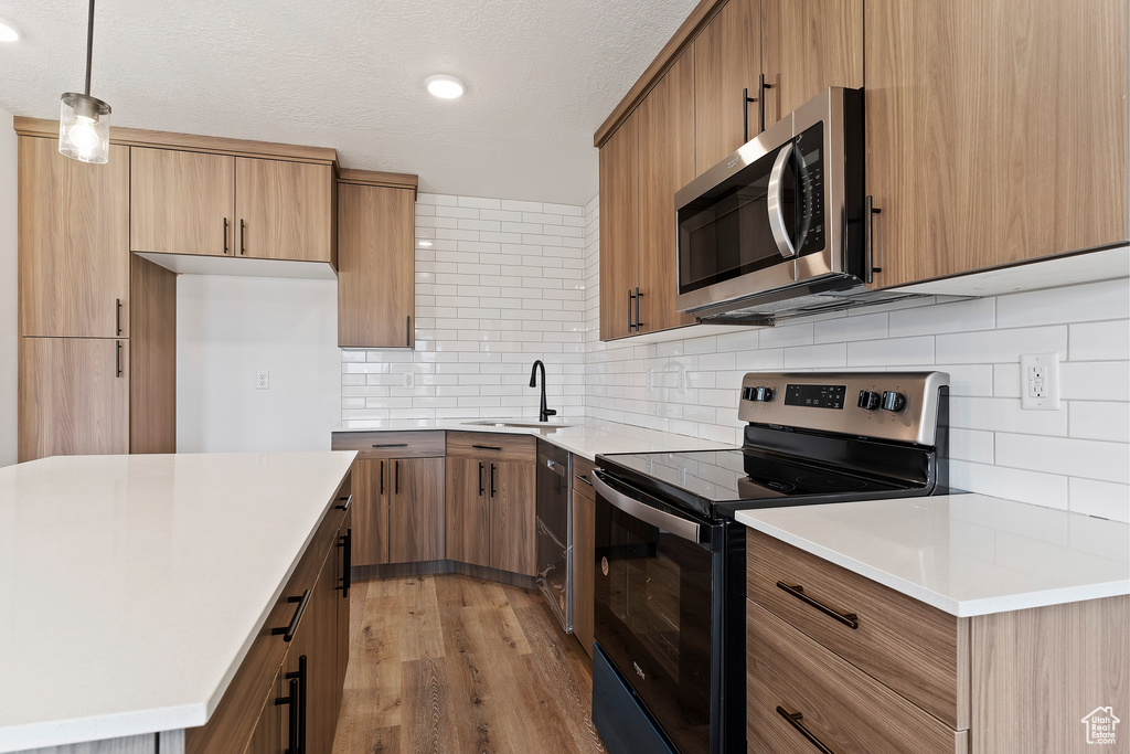 Kitchen featuring a textured ceiling, pendant lighting, appliances with stainless steel finishes, light hardwood / wood-style floors, and sink