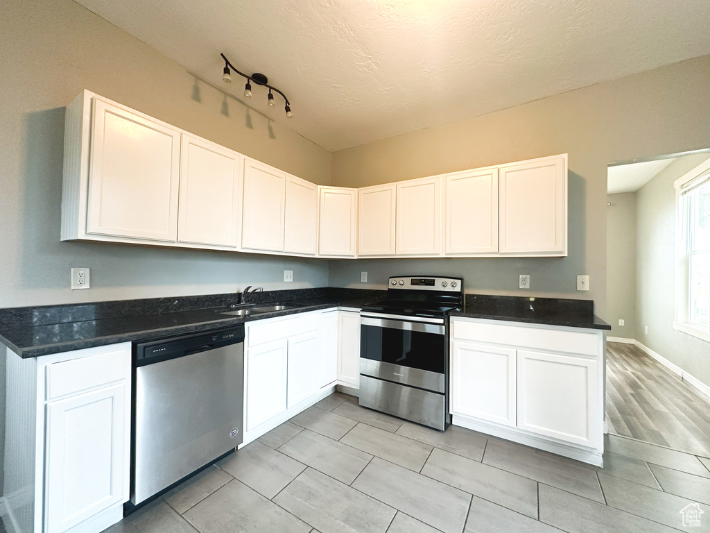 Kitchen featuring a textured ceiling, light hardwood / wood-style floors, stainless steel appliances, sink, and white cabinets