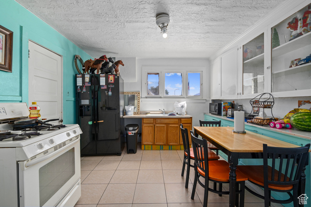 Kitchen with a textured ceiling, white cabinetry, gas range gas stove, light tile patterned flooring, and black fridge