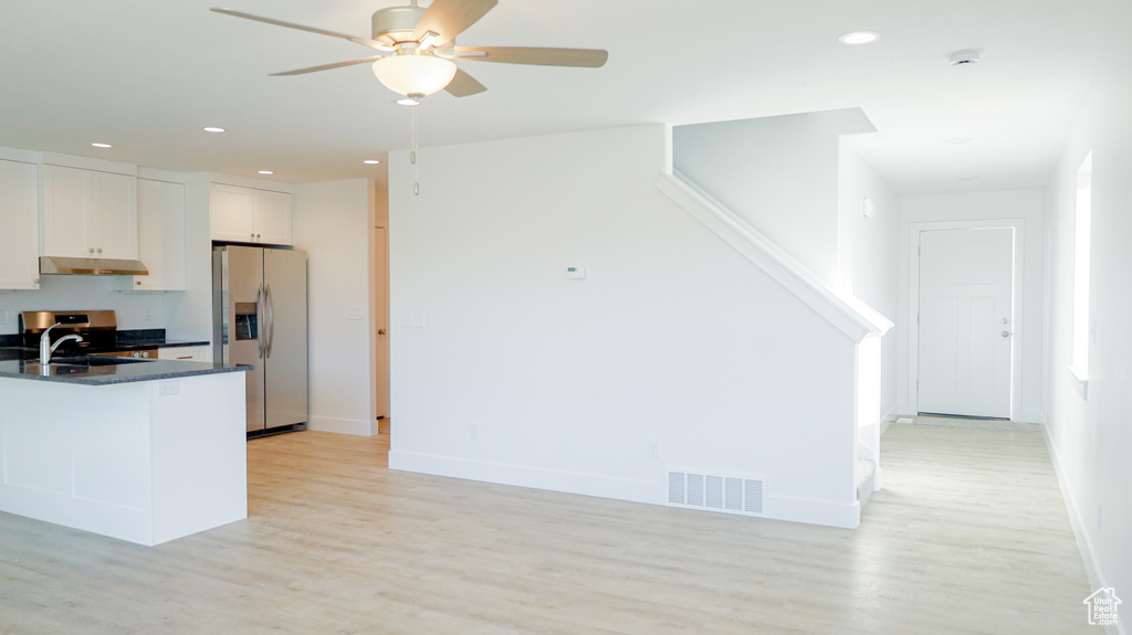 Kitchen with light wood-type flooring, dark stone counters, white cabinetry, stainless steel appliances, and ceiling fan