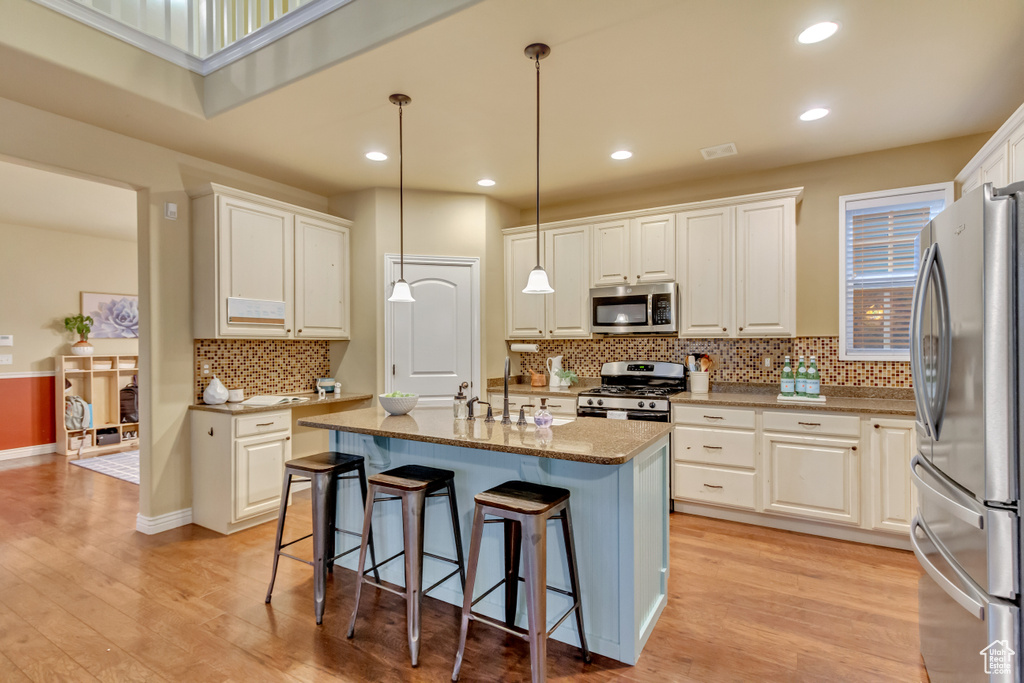 Kitchen featuring light wood-type flooring, white cabinets, appliances with stainless steel finishes, and an island with sink