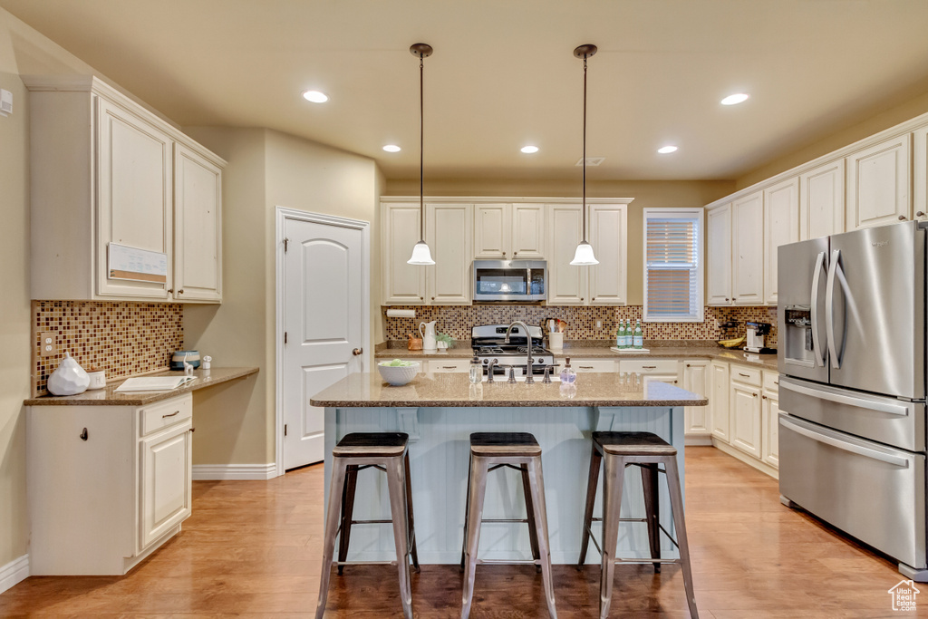 Kitchen with light wood-type flooring, decorative light fixtures, light stone counters, decorative backsplash, and appliances with stainless steel finishes