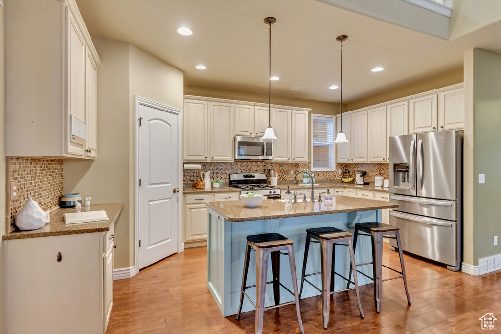 Kitchen with light hardwood / wood-style flooring, decorative light fixtures, stainless steel appliances, and a center island with sink