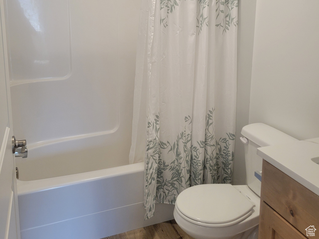 Full bathroom with vanity, shower / bathtub combination with curtain, wood finished floors, and toilet