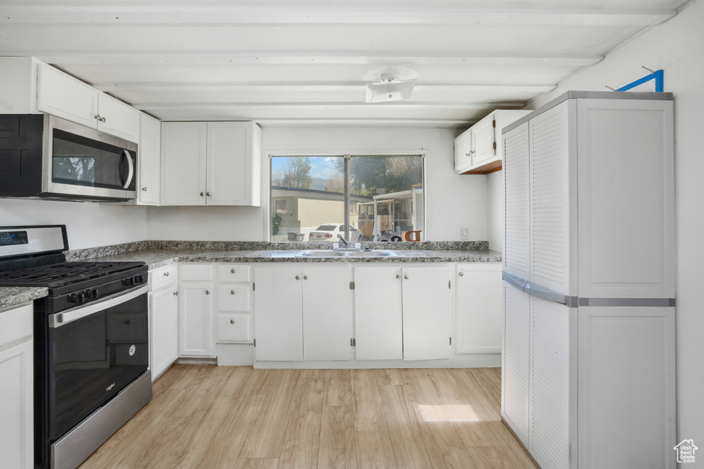 Kitchen featuring appliances with stainless steel finishes, beam ceiling, white cabinets, and light hardwood / wood-style floors