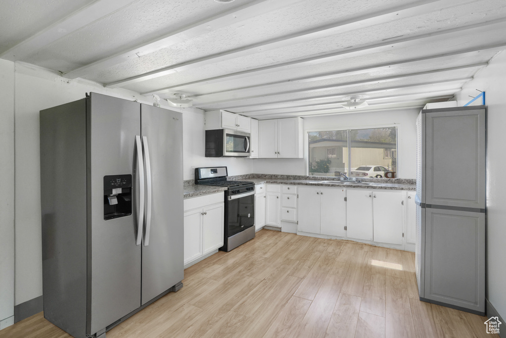 Kitchen with appliances with stainless steel finishes, stone counters, white cabinets, and light hardwood / wood-style floors