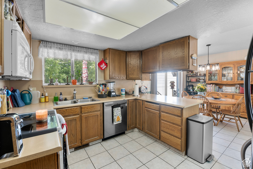 Kitchen with white appliances, hanging light fixtures, kitchen peninsula, sink, and light tile patterned flooring