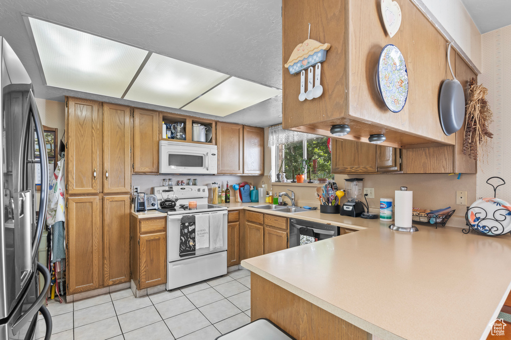 Kitchen featuring kitchen peninsula, sink, appliances with stainless steel finishes, and light tile patterned flooring