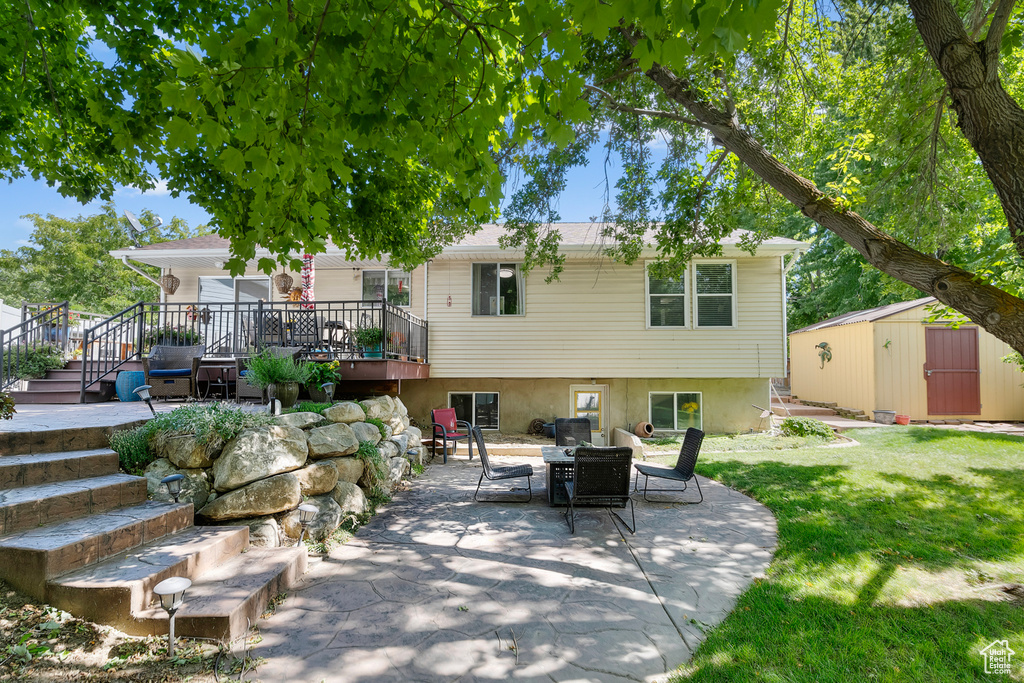 Rear view of house with a wooden deck, a yard, a patio, and a storage shed