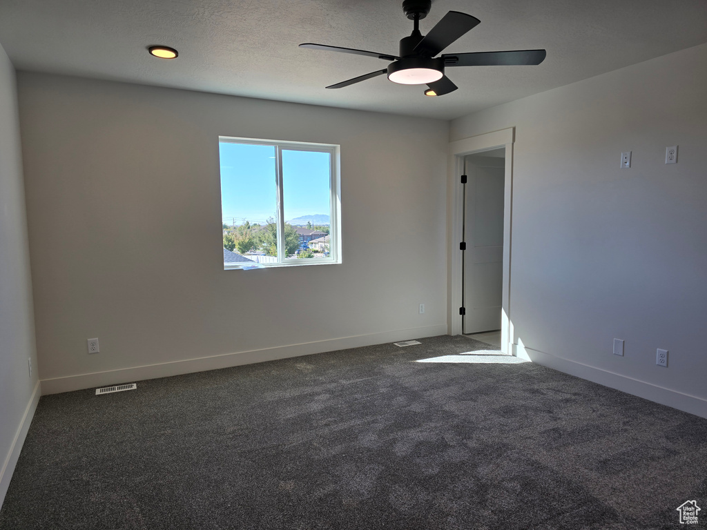 Unfurnished room with ceiling fan and dark colored carpet