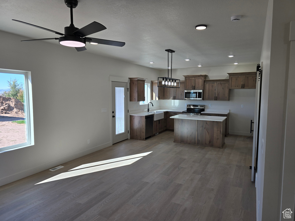 Kitchen with a center island, hardwood / wood-style floors, hanging light fixtures, ceiling fan, and stainless steel appliances