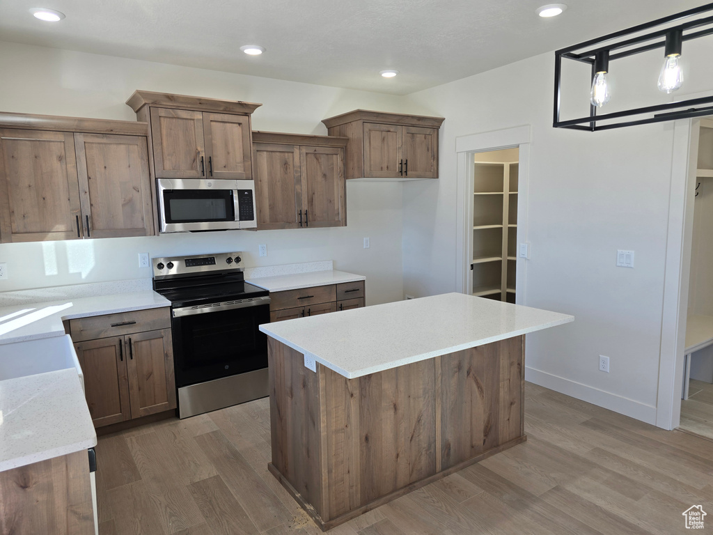 Kitchen with a kitchen island, appliances with stainless steel finishes, light hardwood / wood-style flooring, and decorative light fixtures