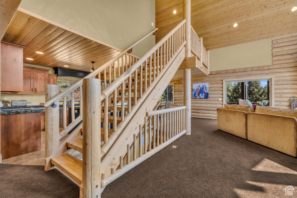 Stairs featuring a towering ceiling, log walls, and wooden ceiling