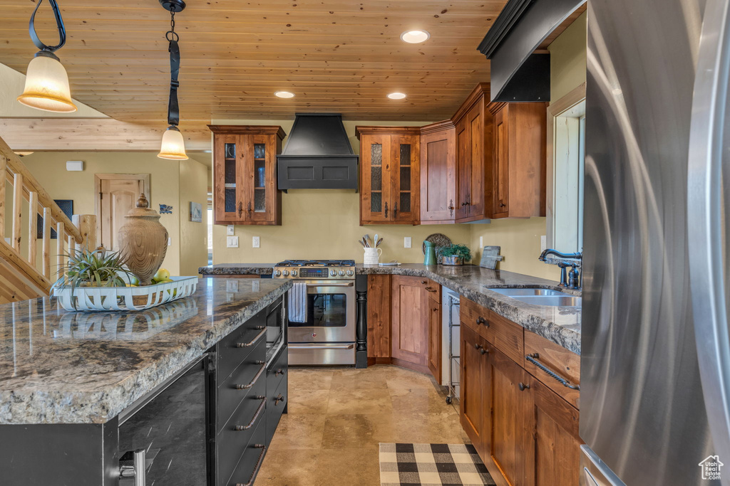 Kitchen with decorative light fixtures, stainless steel appliances, sink, premium range hood, and dark stone counters