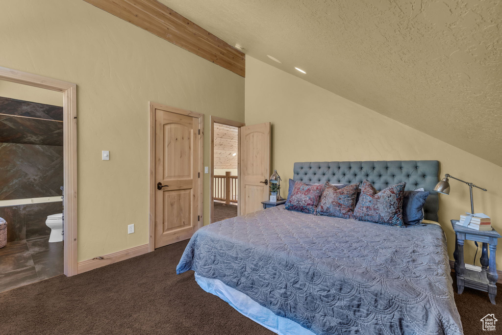 Carpeted bedroom featuring ensuite bath, a textured ceiling, and vaulted ceiling with beams