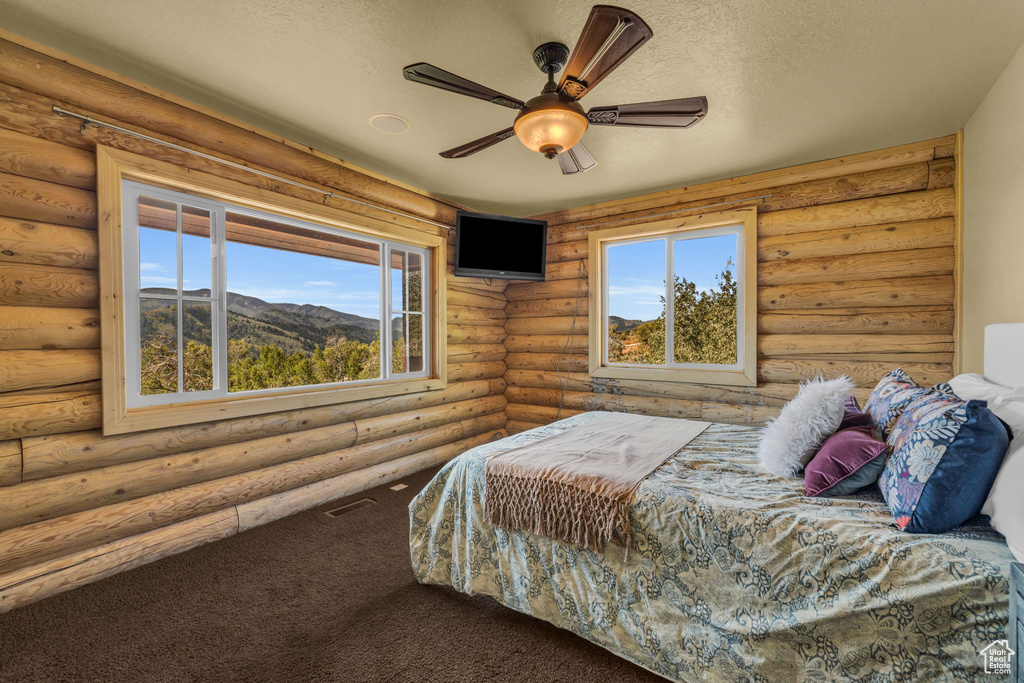 Bedroom featuring log walls, carpet flooring, ceiling fan, and a textured ceiling