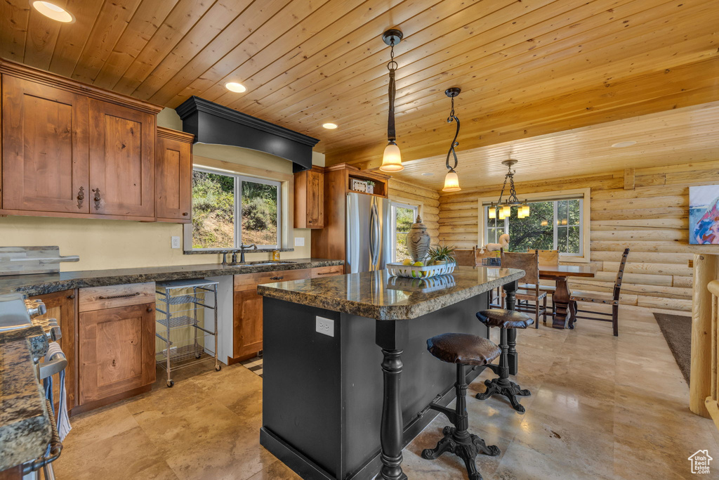 Kitchen with plenty of natural light, a kitchen island, stainless steel refrigerator, and rustic walls