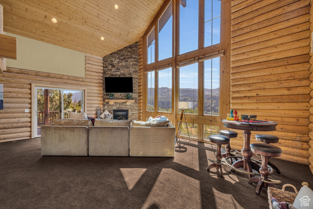 Carpeted living room with rustic walls, a stone fireplace, high vaulted ceiling, and wooden ceiling