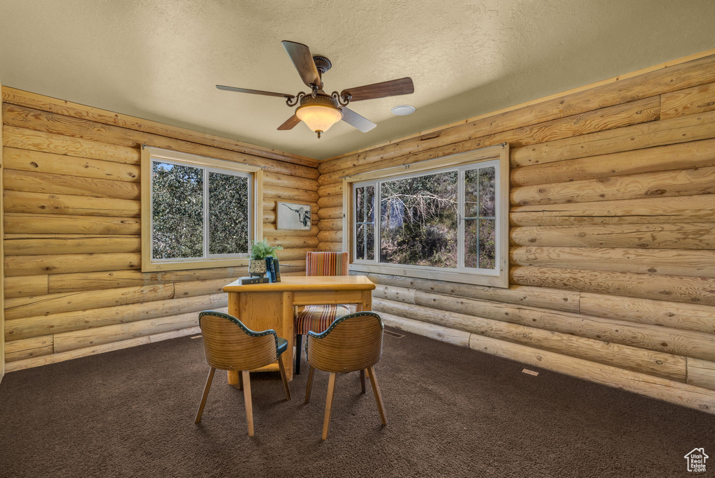 Carpeted dining room featuring a textured ceiling, ceiling fan, and rustic walls