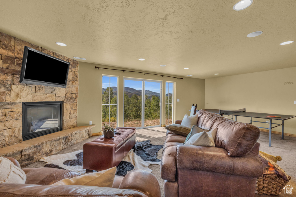 Living room with carpet, a textured ceiling, and a stone fireplace