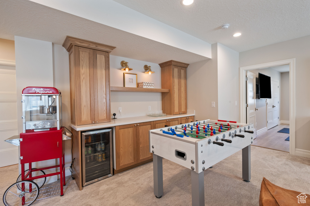 Playroom with a textured ceiling, beverage cooler, bar, and light carpet