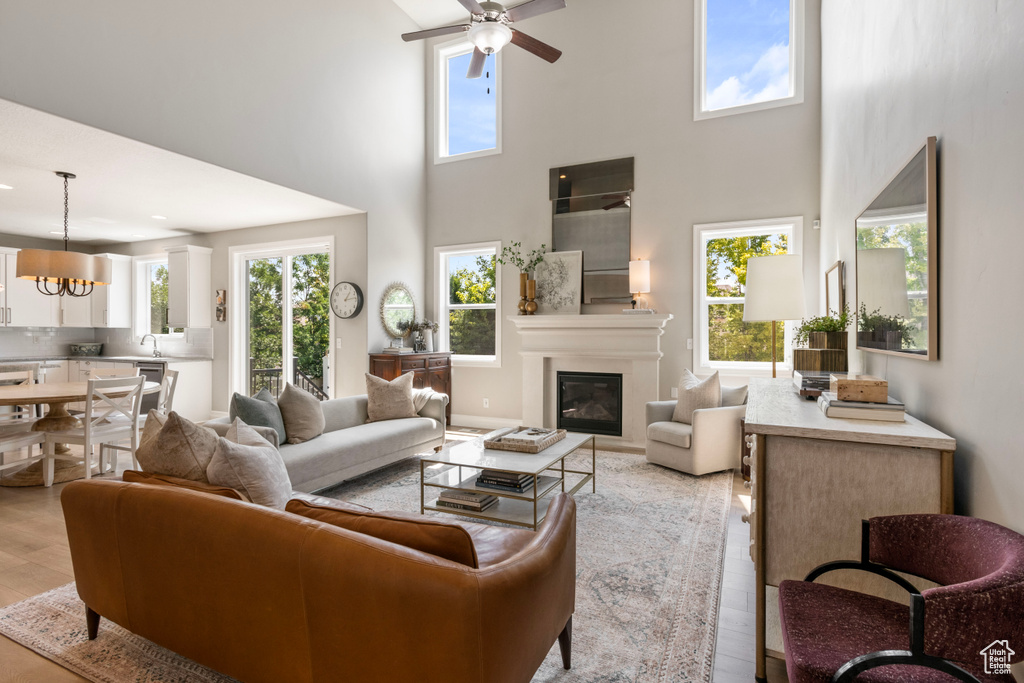 Living room with ceiling fan with notable chandelier, sink, a high ceiling, and light hardwood / wood-style floors