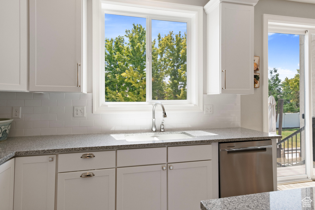 Kitchen with dishwasher, a wealth of natural light, light stone countertops, and white cabinetry