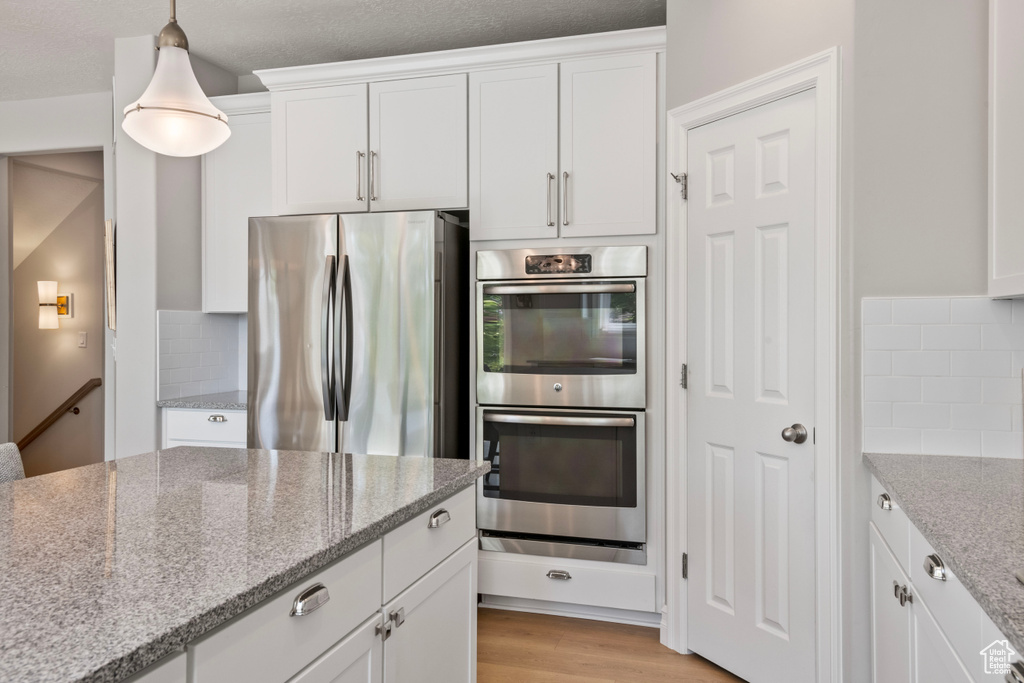 Kitchen featuring pendant lighting, light hardwood / wood-style flooring, stainless steel appliances, white cabinetry, and light stone counters