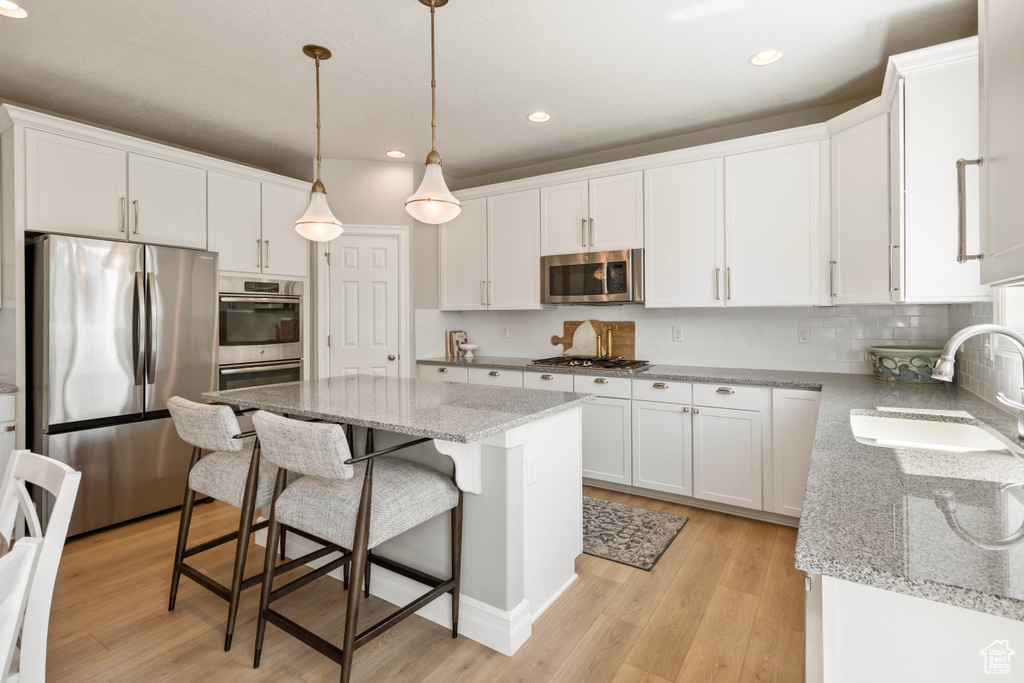 Kitchen with light hardwood / wood-style flooring, appliances with stainless steel finishes, a center island, sink, and white cabinets