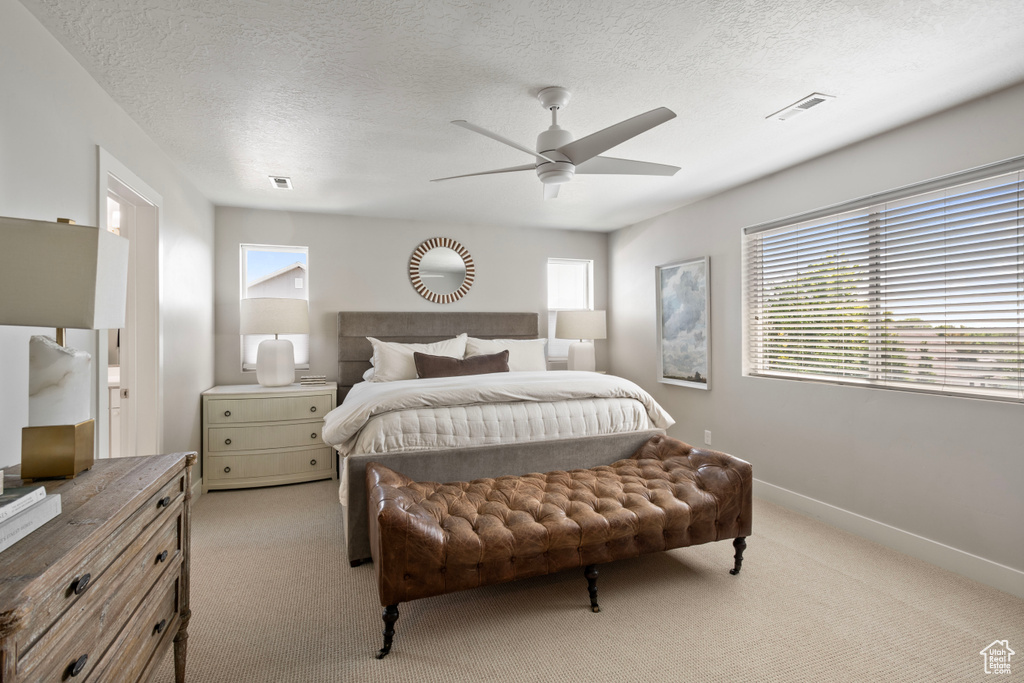 Bedroom with ceiling fan, light colored carpet, and a textured ceiling