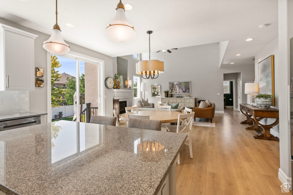 Kitchen with a notable chandelier, light hardwood / wood-style flooring, decorative light fixtures, light stone counters, and white cabinets