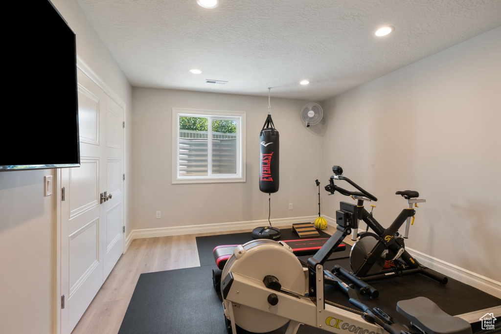 Exercise area with a textured ceiling and light hardwood / wood-style floors