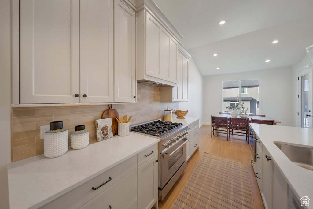 Kitchen featuring white cabinets, light hardwood / wood-style flooring, stainless steel range, vaulted ceiling, and decorative backsplash