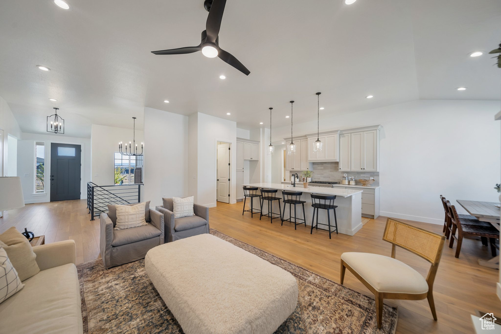 Living room with ceiling fan with notable chandelier, vaulted ceiling, sink, and light wood-type flooring