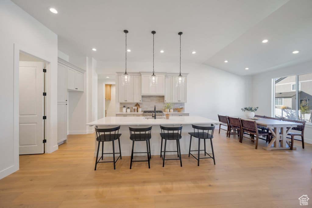 Kitchen featuring light hardwood / wood-style floors, a kitchen island with sink, decorative light fixtures, and white cabinetry