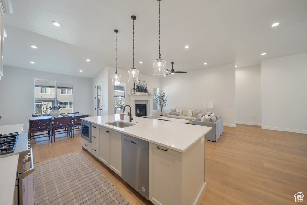 Kitchen featuring a center island with sink, sink, stainless steel appliances, hanging light fixtures, and white cabinets