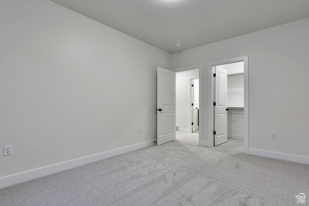 Unfurnished bedroom featuring a spacious closet, light colored carpet, and a closet