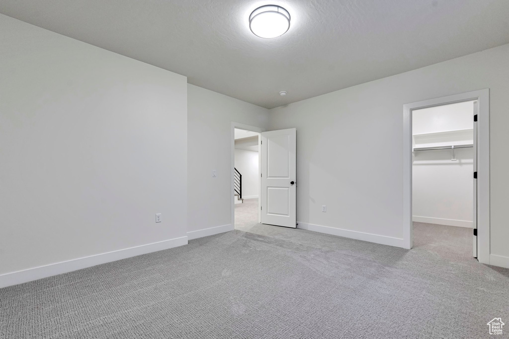 Unfurnished bedroom featuring light carpet, a walk in closet, and a closet